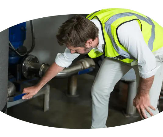 Ein Mann in einer gelben Weste inspiziert ein Rohr auf einer Baustelle.